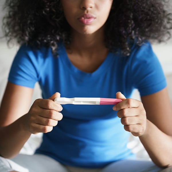 Woman sitting on a bed looking at the results of a pregnancy test.
